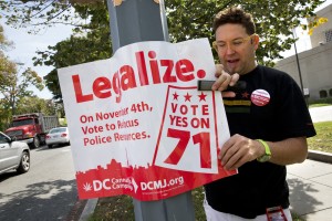 In this photo taken Oct. 9, 2014, Adam Eidinger, chairman of the DC Cannabis Campaign, puts up posters encouraging people to vote yes on DC Ballot Initiative 71 to legalize small amounts of marijuana for personal use, in Washington. On Tuesday, the Washington Post reported on a potential budget deal in the works that would prevent legalization from happening in the nation’s capital. (AP Photo/Jacquelyn Martin)