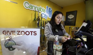In this Tuesday, Dec. 30, 2014, photo, Cannabis City clerk Jessica Mann scans a customer's ID as she rings up a purchase of marijuana at the shop in Seattle. (AP Photo/Elaine Thompson)