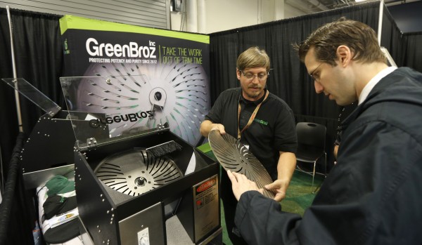 Cullen Raichart, center, CEO of GreenBroz, Inc., shows a prospective customer one of the blades of a mechanical pot trimming machine on display at CannaCon.   (AP Photo/Ted S. Warren)